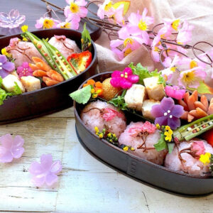 黒い塗りのお弁当箱の中に桜いろのお料理が盛り付けられている